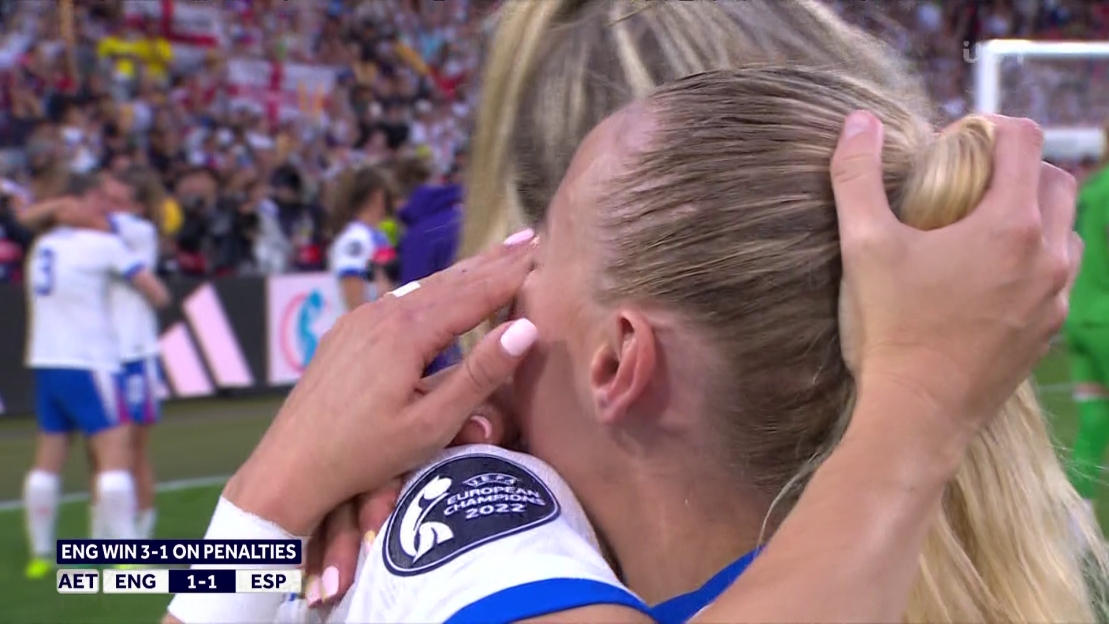 A female soccer player crying and being comforted by a teammate after a penalty shootout win.