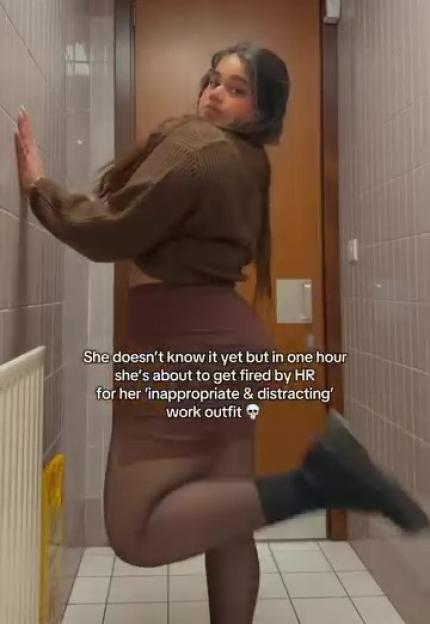 Woman in a brown sweater and skirt posing in a hallway.