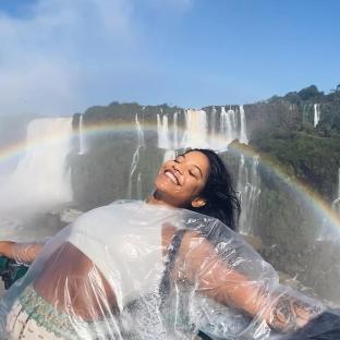 Woman in a plastic poncho smiling in front of a waterfall with a rainbow.