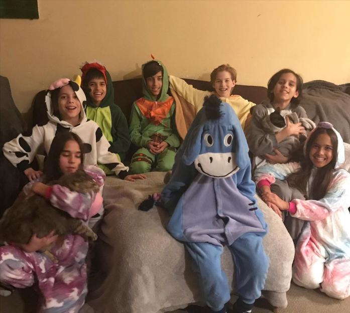 Eight children in animal pajamas on a couch.