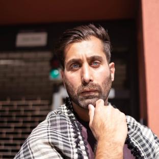 Portrait of a man with blue eyes and a beard, wearing a checkered scarf.