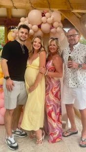 Photo of a pregnant woman with her partner, parents, and a balloon arch.