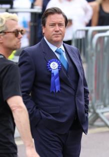 Rufus Jones on the set of Rivals, wearing a suit and blue rosette.