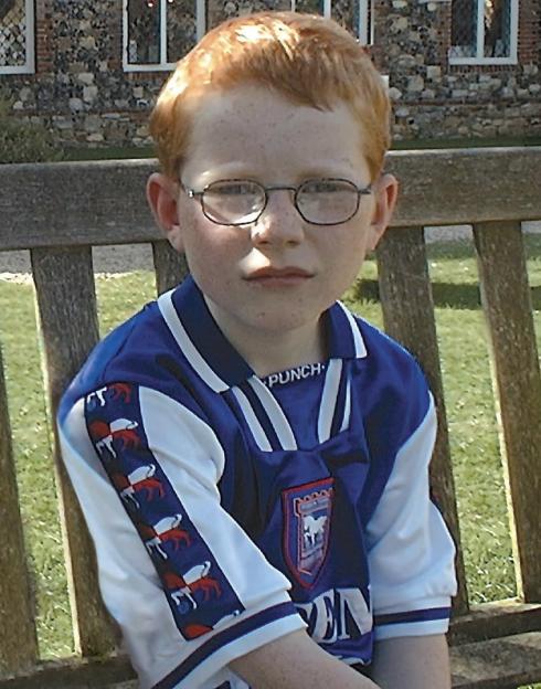 Young boy wearing glasses and a soccer jersey.