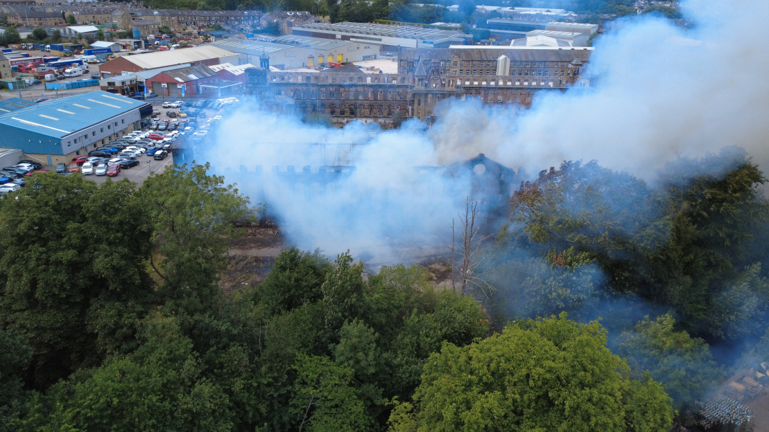 Aerial view of a building fire with smoke billowing over trees and surrounding buildings.