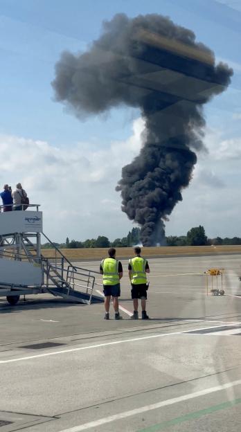 Large plume of black smoke rising from a plane crash at an airport.