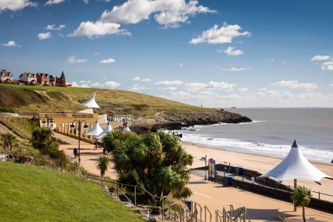 Barry Island seafront, showing gardens, promenade, beach, and houses on a hill.