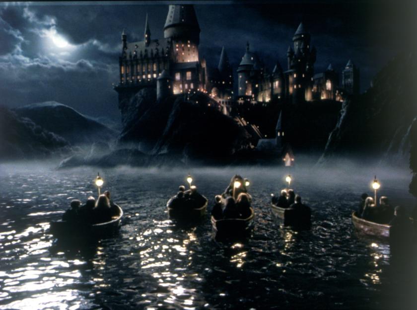 Hogwarts castle at night, seen from across a lake where boats carry students.