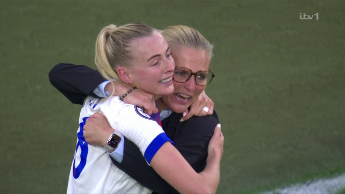 Two women embracing on a soccer field.
