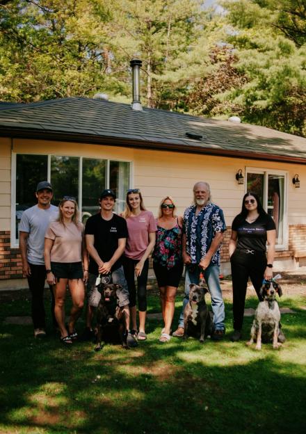 Family portrait in front of their house with three dogs.