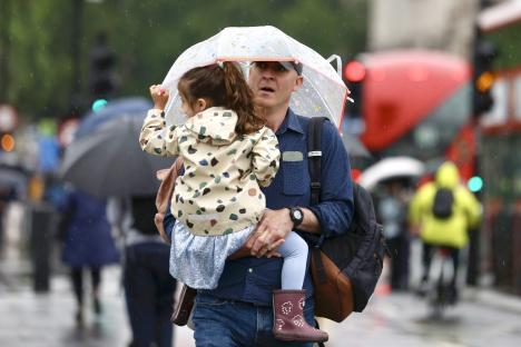 A man carries a young child under a small umbrella in heavy rain.