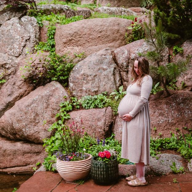 Pregnant person standing in front of a rock garden.