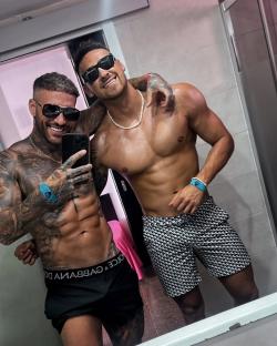 Two shirtless men in sunglasses taking a selfie.
