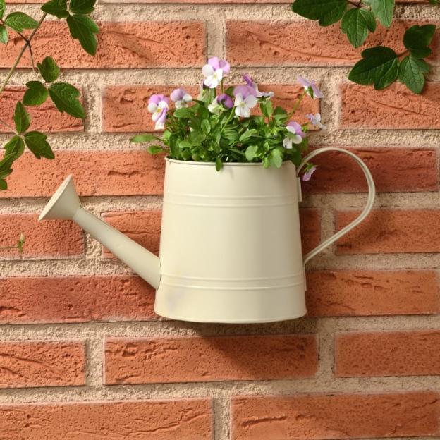 Cream-colored watering can with pansies, mounted on a brick wall.