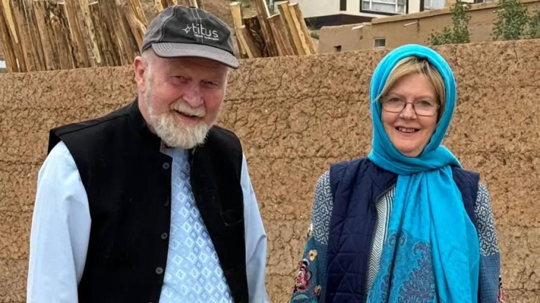 Photo of a man and woman standing in front of a mud-brick wall.