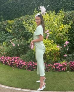 Woman in a light green dress and hat, standing in a garden.