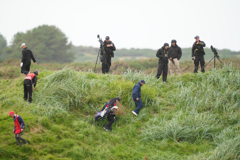 Golfers and photographers on a grassy hill.
