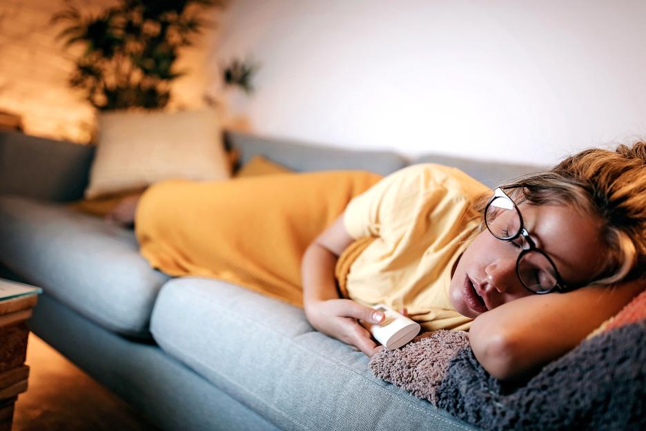 Woman asleep on couch holding remote.