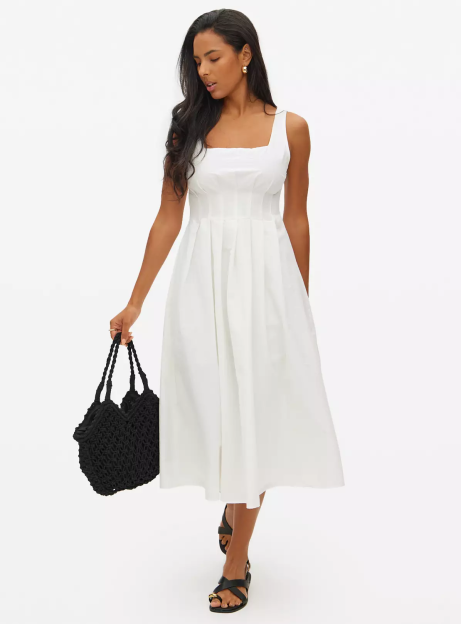 Woman in white midi dress and black sandals carrying a black tote bag.