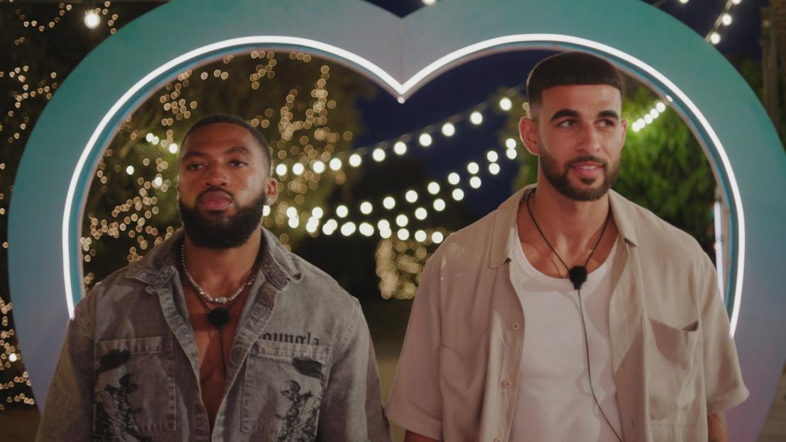 Two men walking toward the camera, illuminated by string lights.