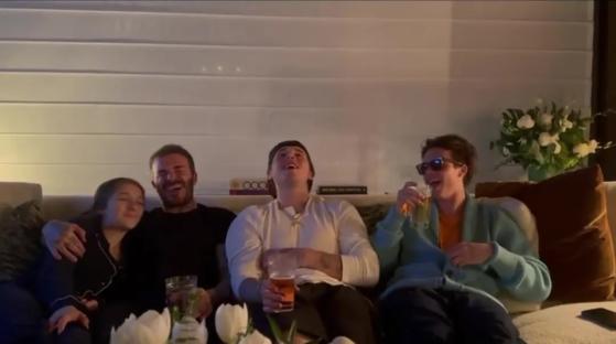 David Beckham and three of his children laughing together on a couch.