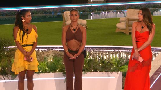 Three women stand on a stage, looking concerned.