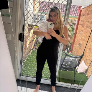 Woman in black jumpsuit holding baby and taking a selfie.