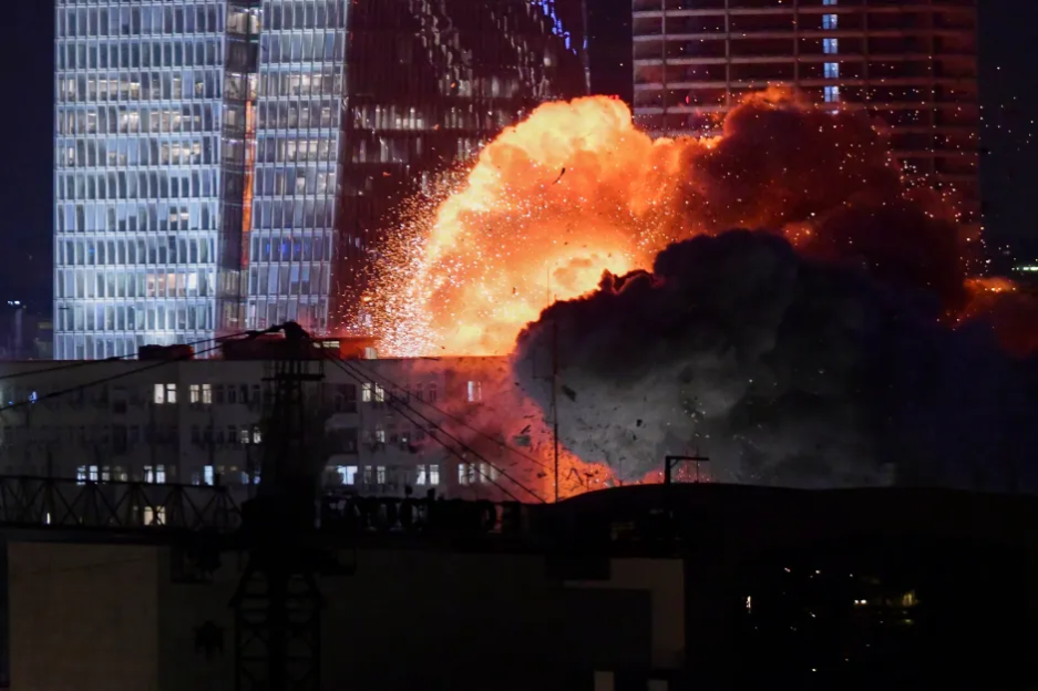 Large explosion near buildings at night.