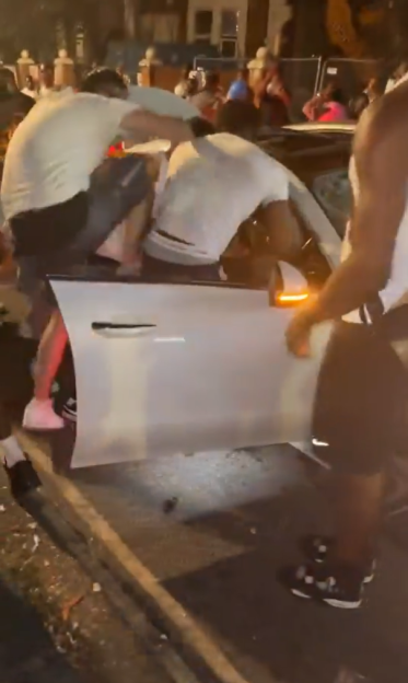 A gang surrounding a car, climbing on it.
