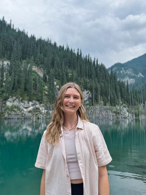 Woman smiling in front of a lake and mountain range.