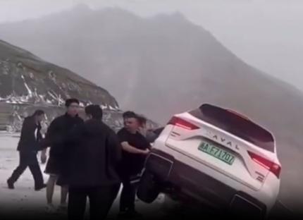 People pushing a car back from the edge of a cliff.