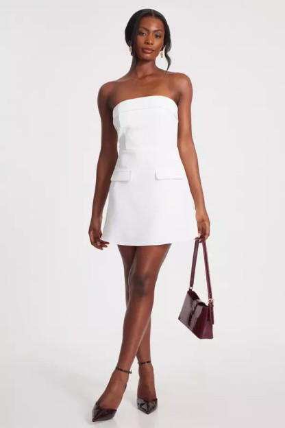 Woman in white strapless mini dress and dark burgundy heels and handbag.