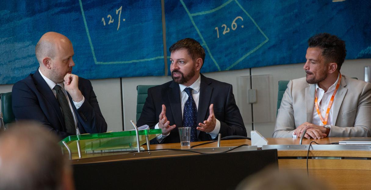 Three men at a parliamentary screening discussing teen smartphone use.