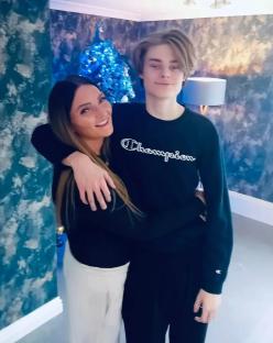 Woman and teen boy embracing in front of a Christmas tree.