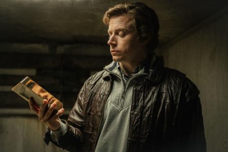 Man in a brown leather jacket examining a gold bar.