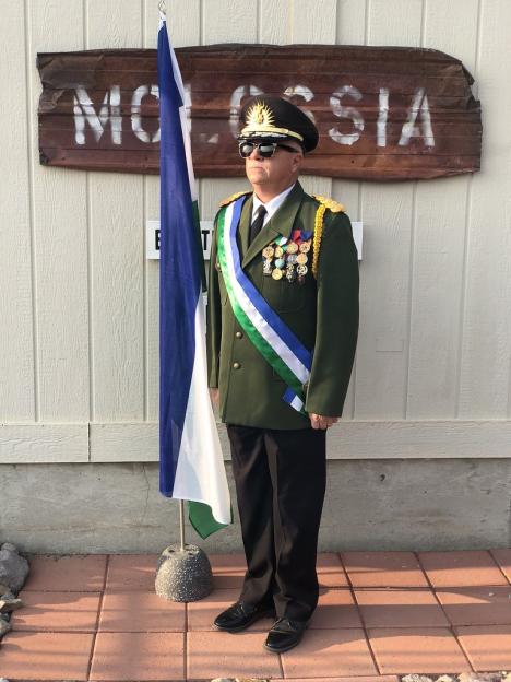 Person in military uniform standing by a flagpole and a sign that says