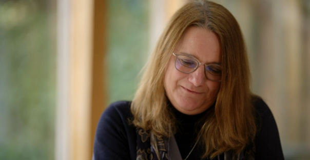 A woman with long brown hair and glasses looking down.