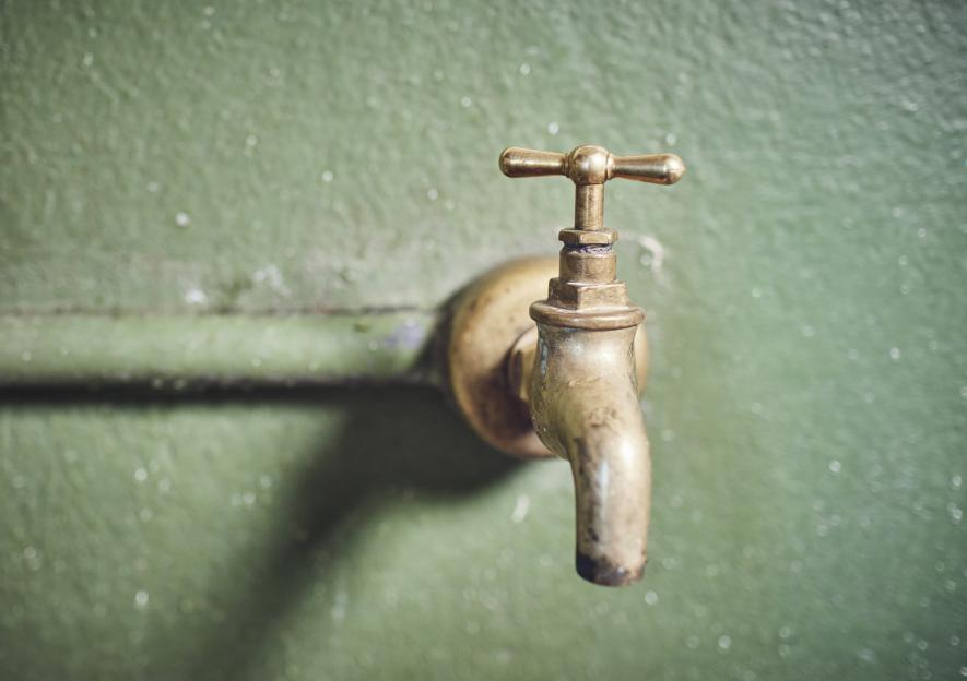 Close-up of an old brass faucet on a green wall.