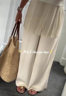 Person wearing a cream-colored fringe top and sandals.