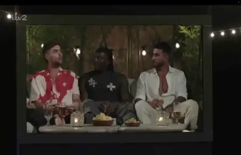 Three men sitting outdoors at night, talking and drinking.