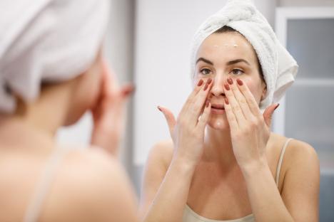 Woman applying face cream in bathroom mirror.