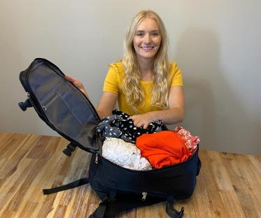 Woman packing clothes into a black backpack.