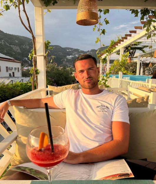 Man sitting outdoors at a restaurant with a drink and menu.