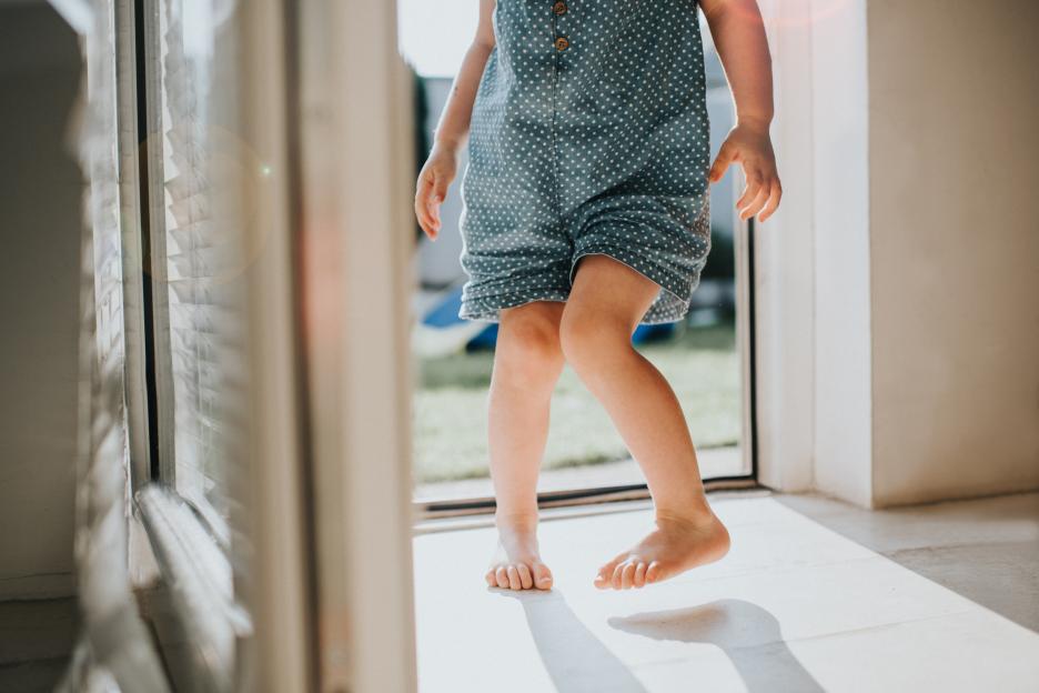 Barefoot toddler's legs in a blue polka dot outfit.