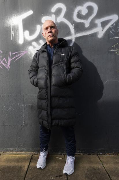 A man in a black puffer jacket stands against a graffiti-covered wall.