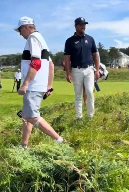 Two golfers walking across a grassy area.