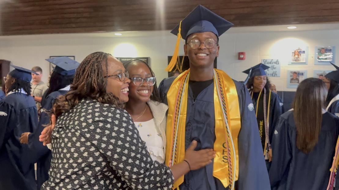 A graduate in cap and gown poses with family.