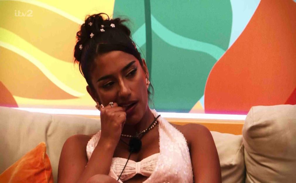 A woman sits on a couch, looking pensive.