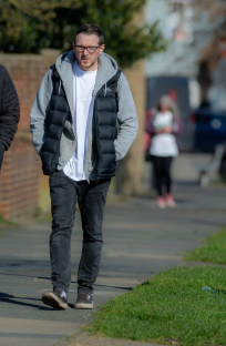 Man wearing glasses and a puffer vest walking down a sidewalk.