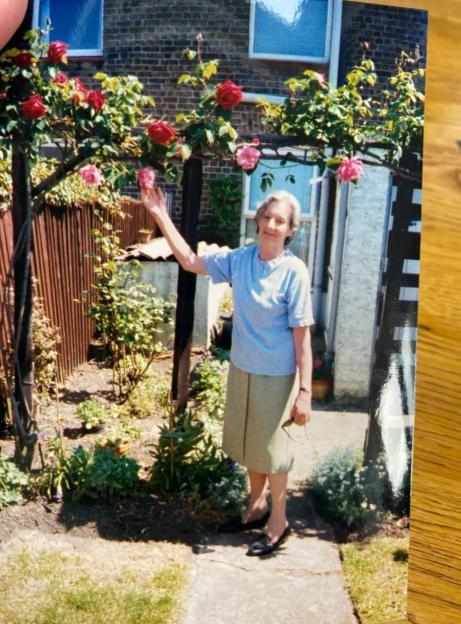 Photo of a woman standing in her garden next to a rose trellis.